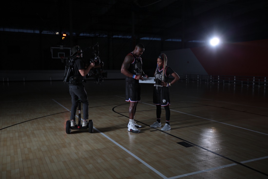 Camera operator filming athletes on a basketball court.