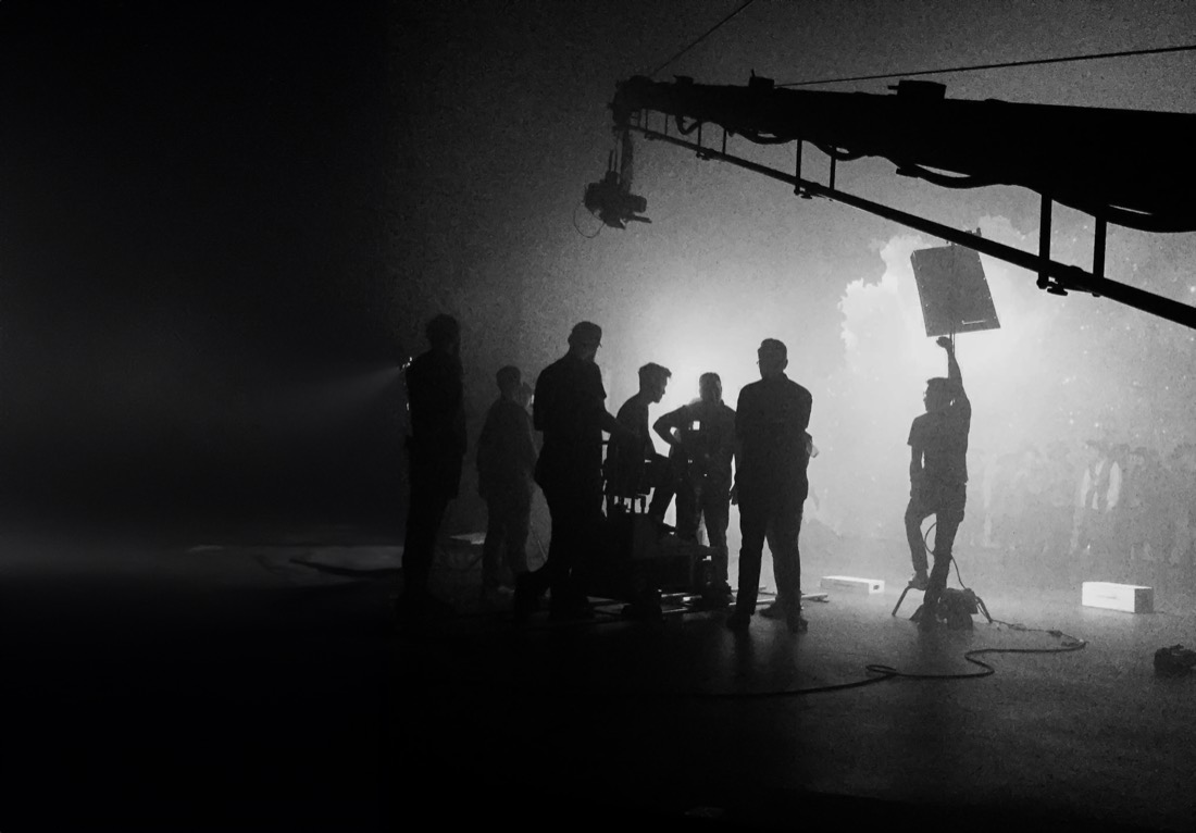 Silhouetted production crew working in a hazy studio.