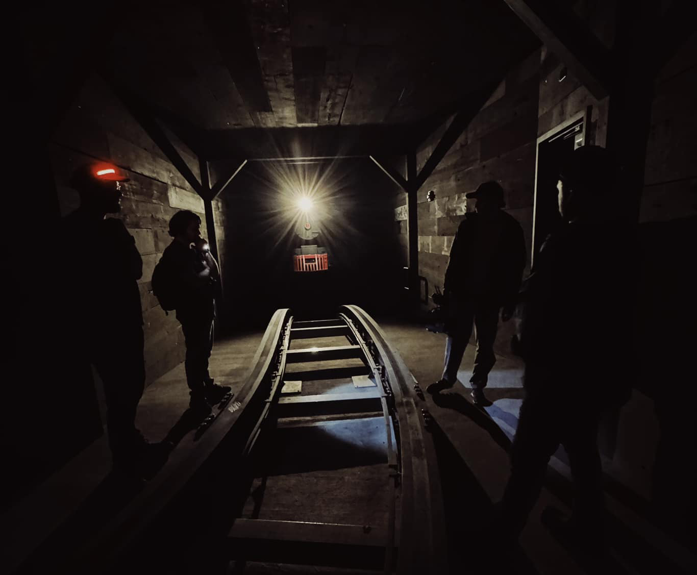 Crew scouting a dark coaster tunnel lit only by a mine headlamp