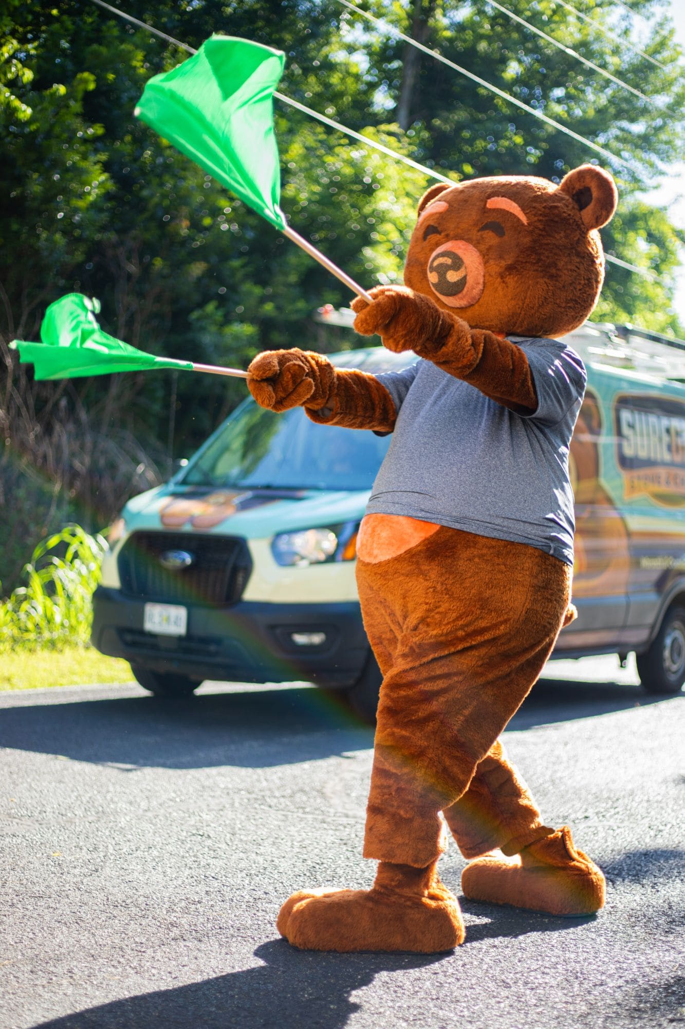 SureGlow bear mascot waving green flags in front of a branded van