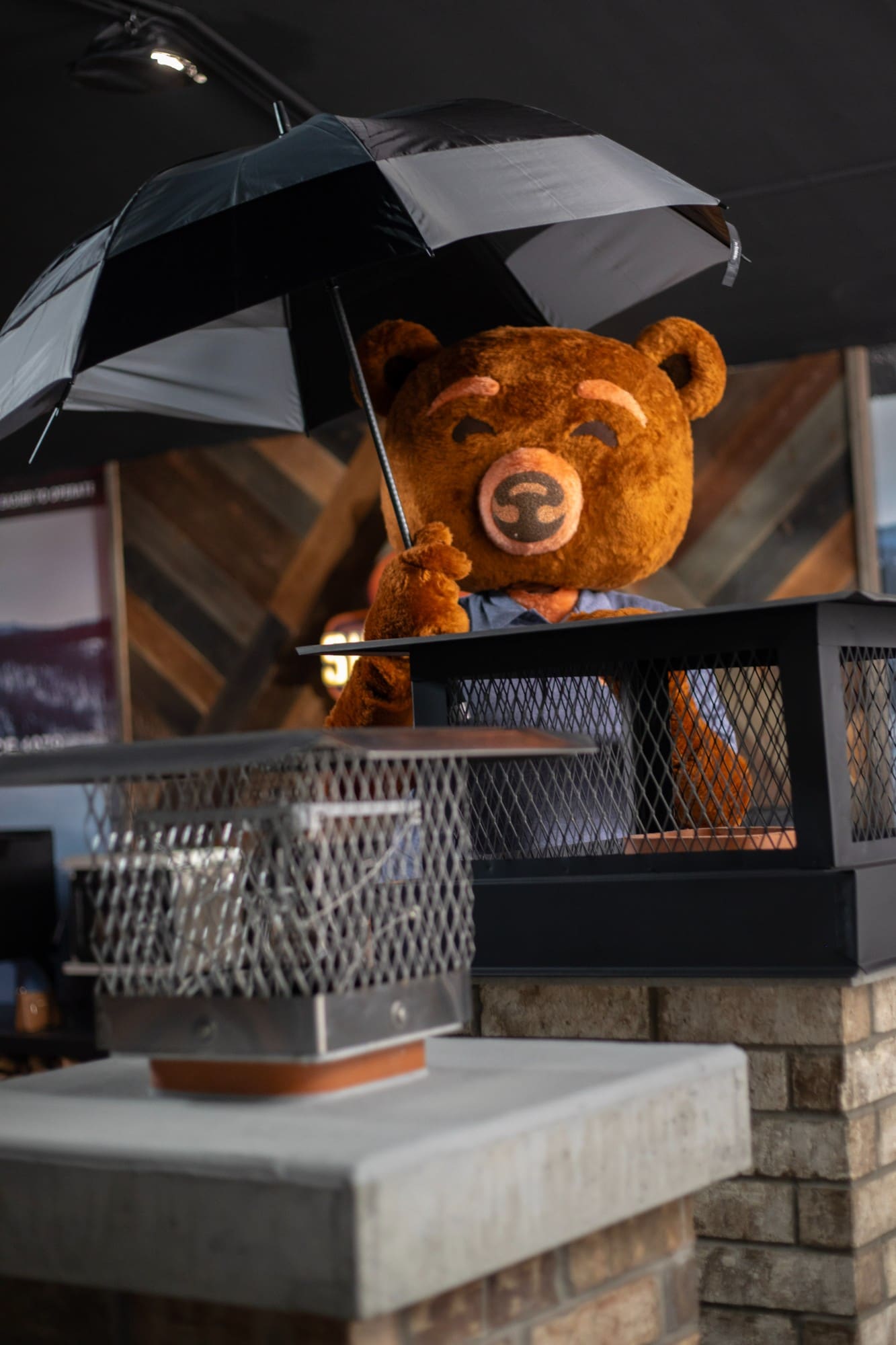 SureGlow bear mascot holding an umbrella next to a chimney display