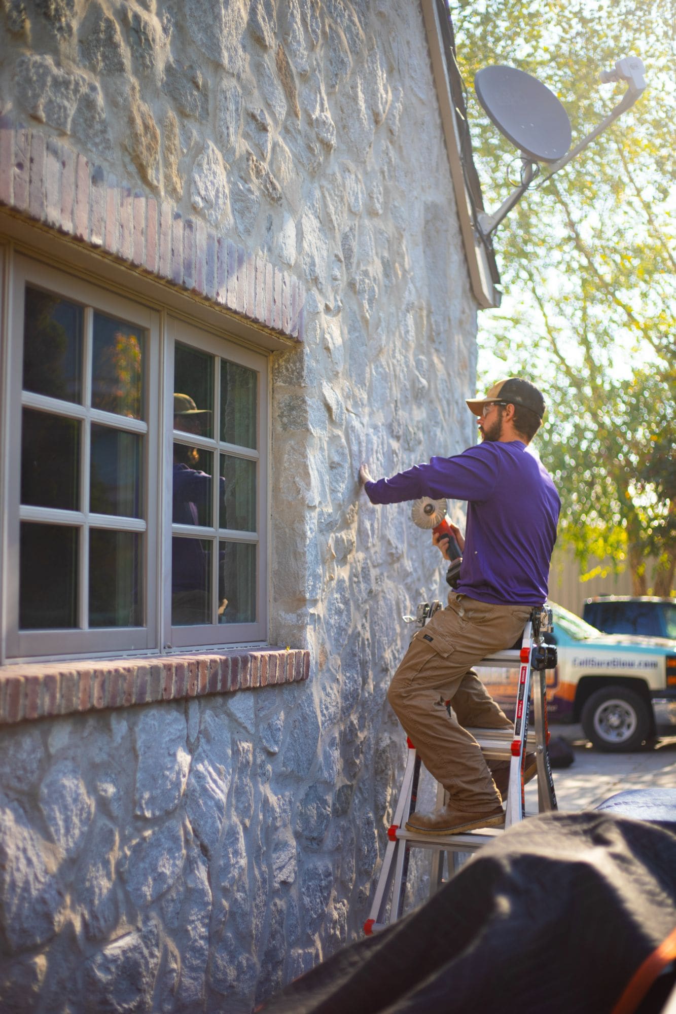 SureGlow technician servicing a stone-faced exterior from a ladder