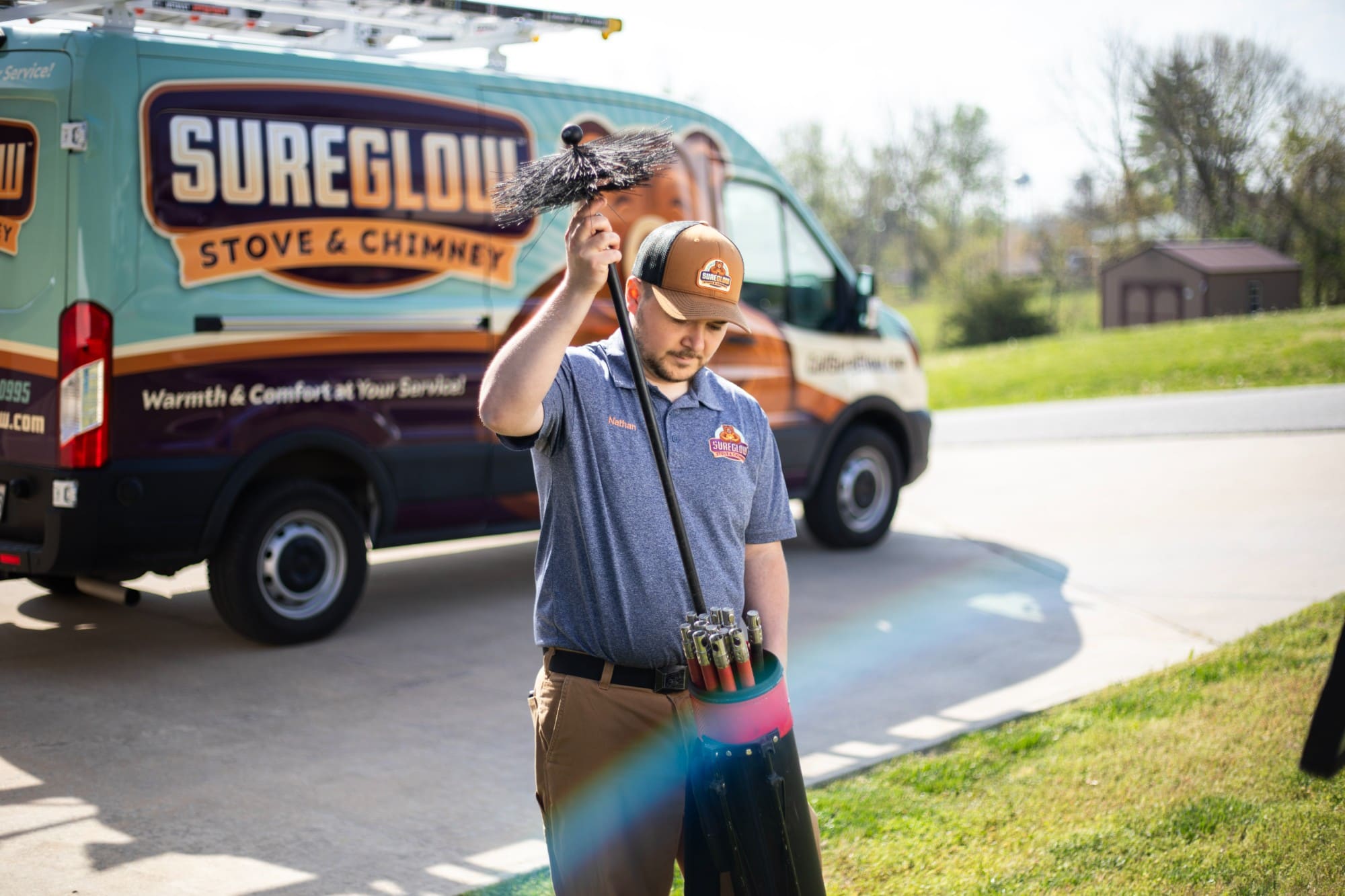 SureGlow technician carrying chimney brushes in front of the branded service van